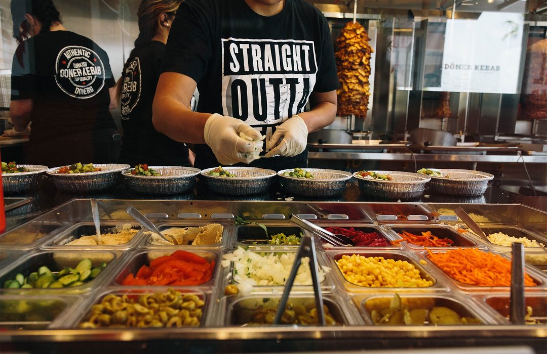 DonerG employee preparing fresh Mediterranean bowls in front of authentic Turkish döner rotisseries.