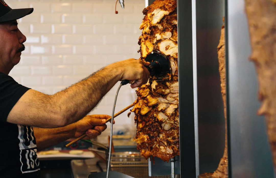 Fresh chicken döner being sliced from a vertical rotisserie at DonerG in Orange County.