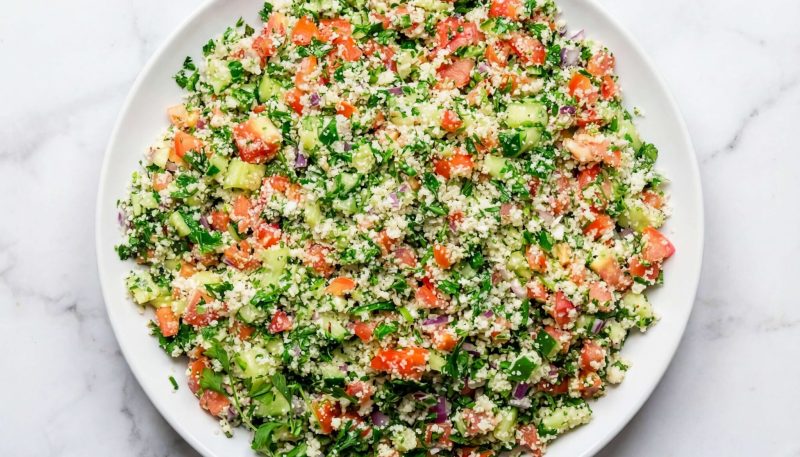 mediterranean cauliflower salad with fresh herbs, tomatoes, and cucumbers in a bowl