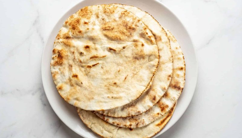 homemade pita bread stacked on a plate, soft and lightly toasted flatbread