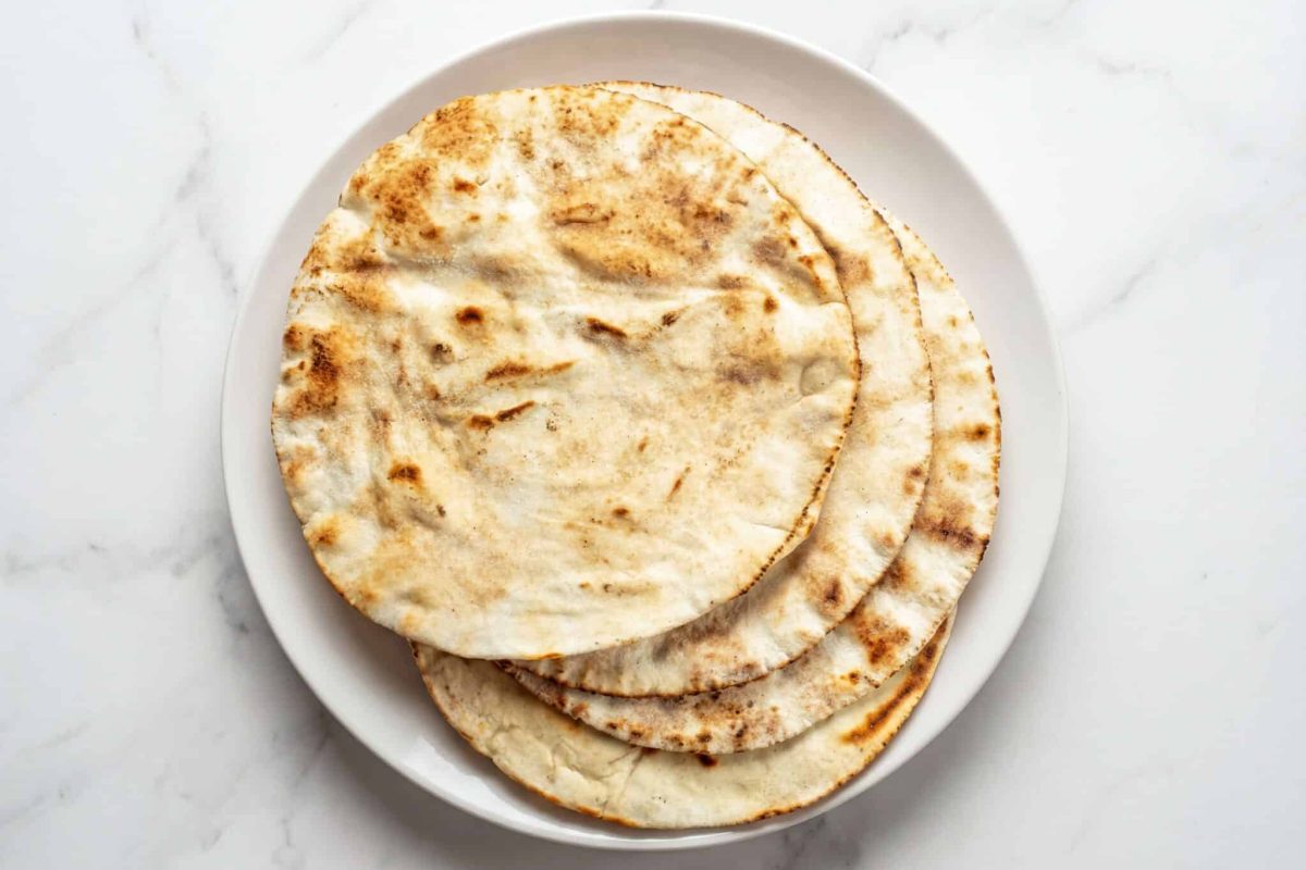 homemade pita bread stacked on a plate, soft and lightly toasted flatbread
