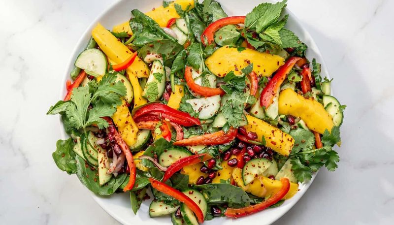 Mediterranean-style mango salad with spinach, cucumbers, herbs, and fresh vegetables