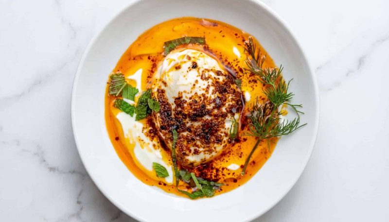 turkish poached eggs with yogurt and chili oil (cilbir) served in a white bowl